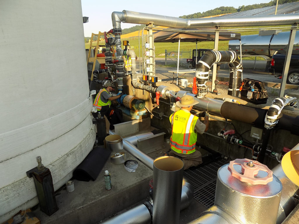 Photo of workers at Liquid and Gaseous Waste Operations addressing two sections of piping to prepare for winter weather