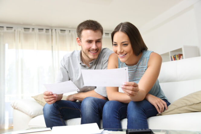 Happy,Young,Couple,Looking,And,Checking,Bills,On,A,Couch