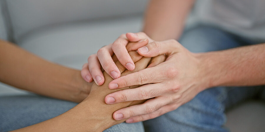 Two,Loving,Couple,Holding,Hands,,Sitting,Together,On,Sofa,At